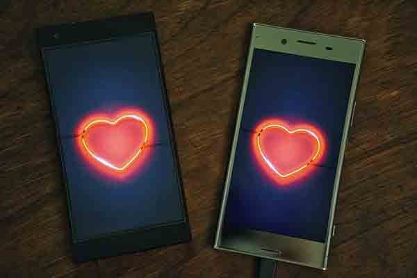 dois celulares sobre mesa de madeira. cada um com imagem de coração neon na tela