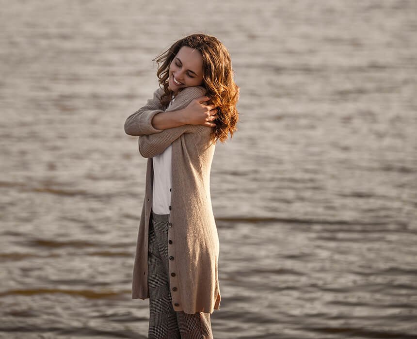 imagem de mulher se abraçando ao lado do mar