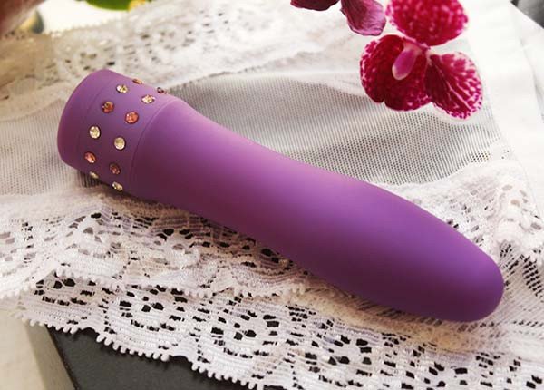 foto vibrador pequeno roxo sobre calcinha branca de renda próximo a flores roxas mini orquidea