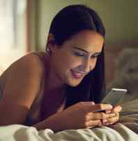 mulher de bruços na cama vendo mensagens pelo celular