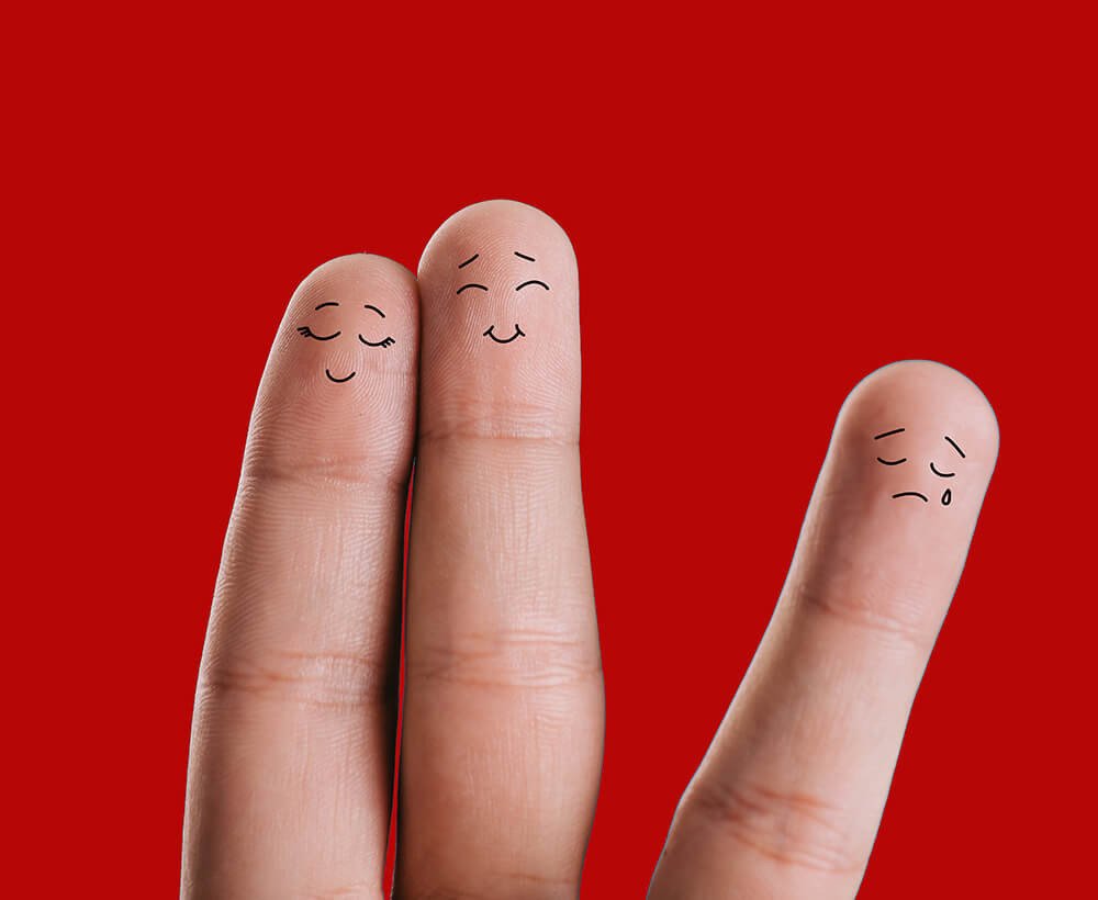 três dedos da mão pintados com desenho de carinhas simbolizando um relacionamento trisal