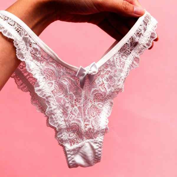 mão feminina segurando calcinha de conjunto de lingerie branca em renda com soutien de bojo modelo strappy