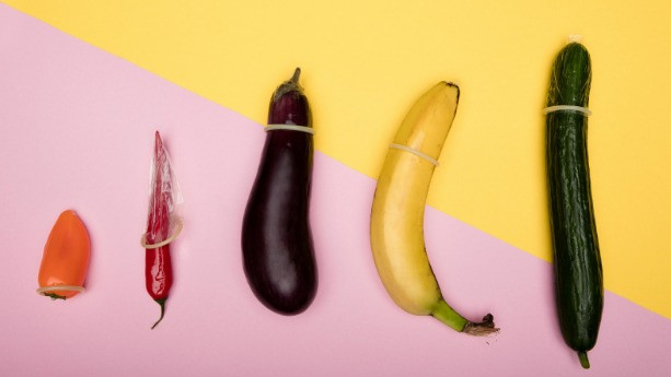 Extensor peniano representado de forma ilustrativa com preservativos em diferentes frutas e vegetais, simbolizando tamanho, segurança e comparação de métodos para aumento peniano.
