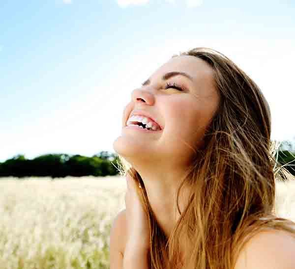 mulher branca sorrindo em lugar com vegetação de campo